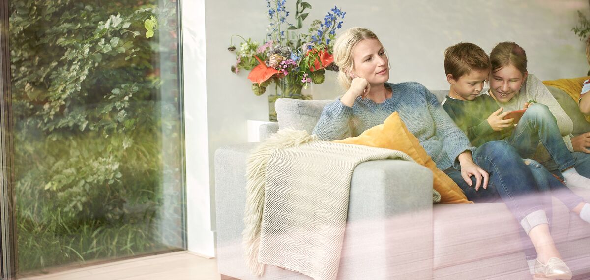 Family relaxing in sofa behind big glass window.