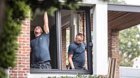 Doi instalatori montează profile noi din aluminiu într-o casă renovată.