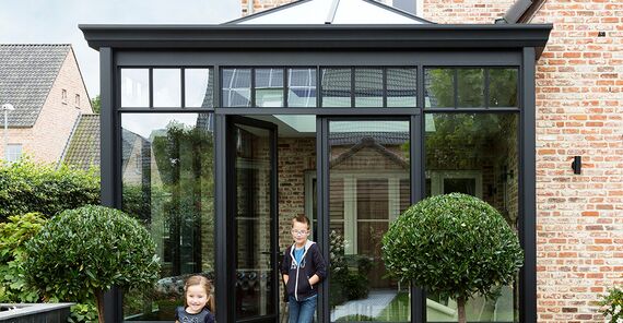 Children playing in the garden in front of black Reynaers Aluminium conservatory.