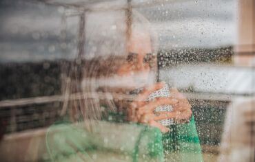 Woman drinking coffee behind glass window on a rainy day.